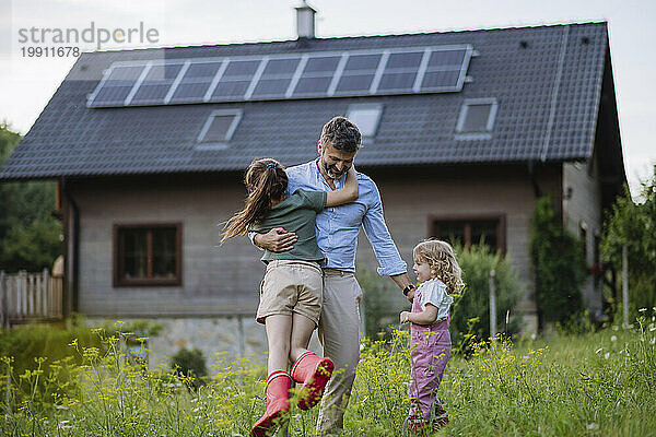Vater und Töchter vergnügen sich vor ihrem Familienhaus mit Sonnenkollektoren auf dem Dach