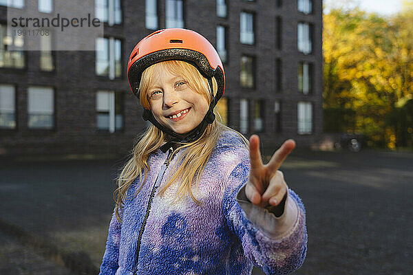 Lächelndes Mädchen mit Helm gestikuliert mit der Hand ein Friedenszeichen