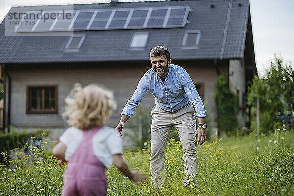 Kleine Tochter rennt zum Vater vor dem Haus ihrer Familie mit Sonnenkollektoren auf dem Dach