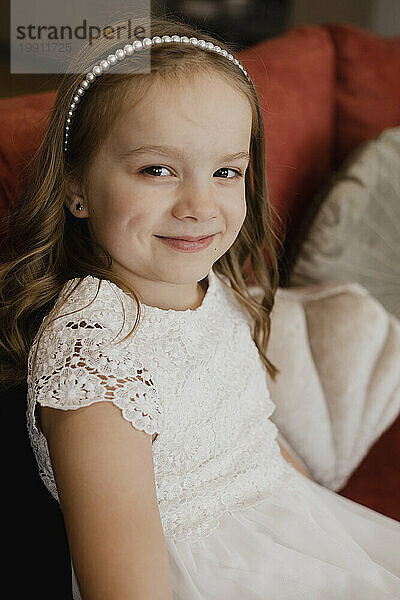Smiling girl wearing white dress and sitting on sofa