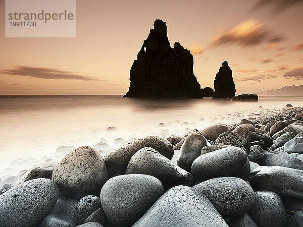 Portugal  Madeira  Porto Moniz  Langzeitbelichtung eines felsigen Strandes in der Abenddämmerung mit der Silhouette eines Meeresstapels im Hintergrund