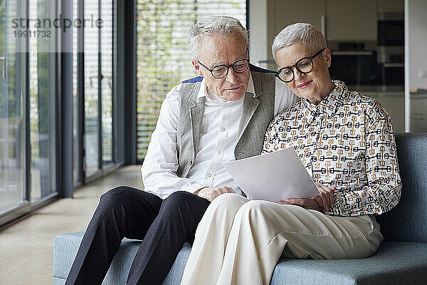 Älteres Paar sitzt zu Hause auf der Couch und liest Dokument