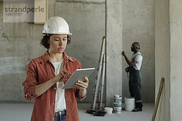 Junger Ingenieur nutzt Tablet-PC mit Kollegen im Hintergrund auf der Baustelle