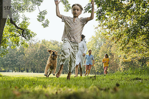 Verspielter Junge rennt mit Hund und Familie auf Gras im Park