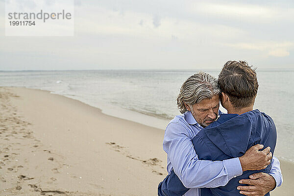 Liebevoller Vater umarmt Sohn am Strand