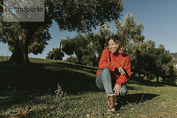 Glückliche Frau kauert an einem sonnigen Tag im Olivenfeld