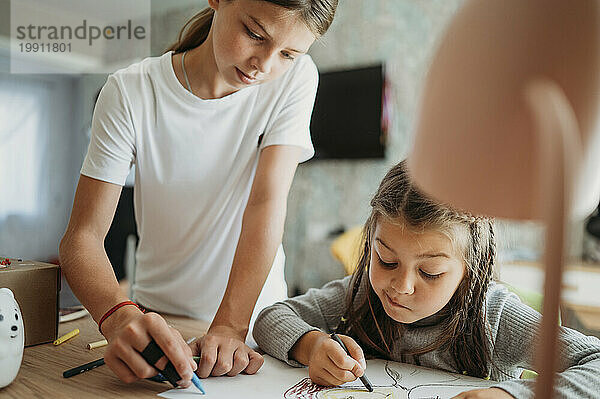 Mädchen hilft Schwester beim Zeichnen zu Hause