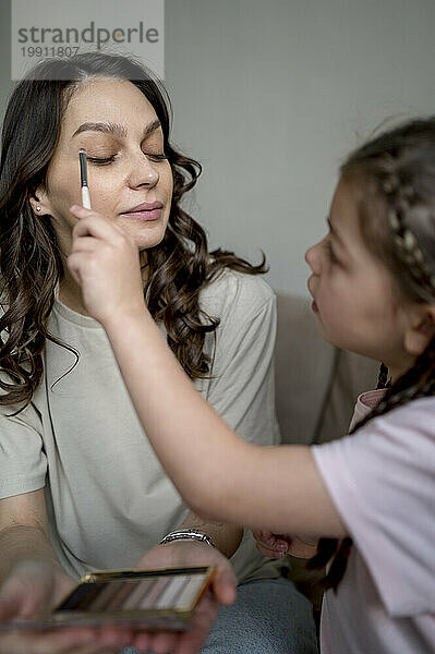 Girl applying eye make-up on mother at home