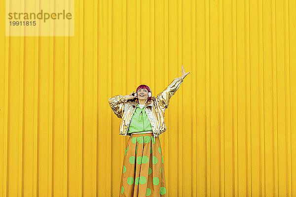 Lächelnde Frau mit kabellosen Kopfhörern und Spaß vor der gelben Wand