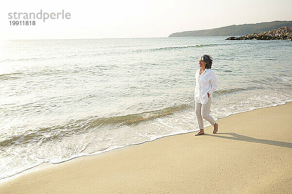Glückliche reife Frau  die an einem sonnigen Tag am Strand spaziert