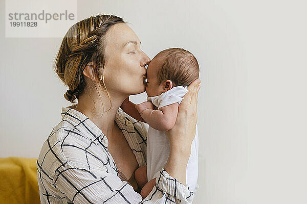 Liebevolle Mutter küsst neugeborenen Sohn auf die Stirn