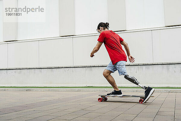 Junger Mann mit Beinprothese fährt Skateboard am Fußweg