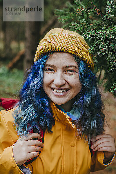 Glückliche Frau mit Strickmütze und Rucksack im Wald