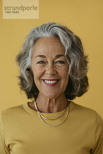 Lächelnde ältere Frau mit kurzen Haaren vor gelbem Hintergrund