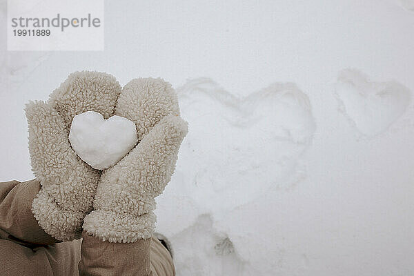Woman wearing gloves and holding heart shaped snow in winter