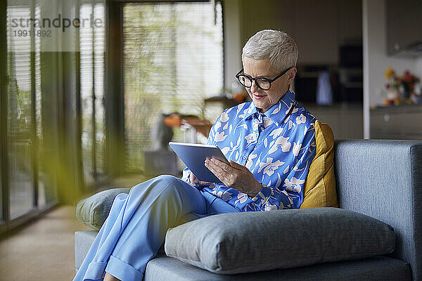 Ältere Frau sitzt zu Hause auf der Couch und benutzt einen Tablet-PC