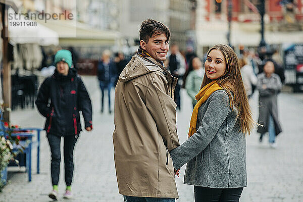 Lächelndes Paar  das Händchen haltend auf der Straße über die Schulter schaut
