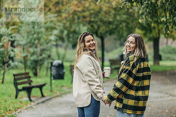 Lächelnde Freunde halten Händchen und gehen im Herbstpark spazieren