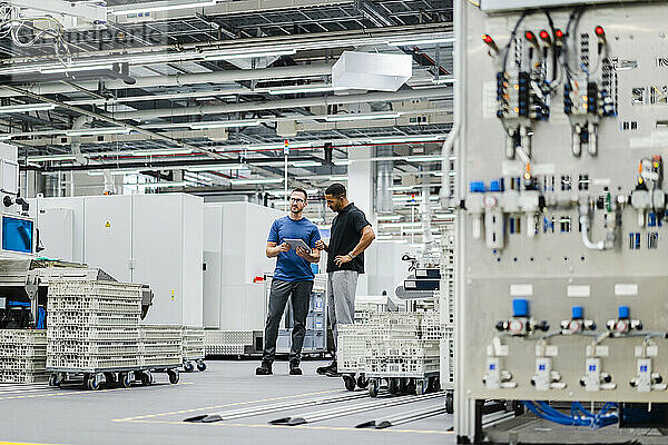 Zwei Kollegen mit digitalem Tablet stehen in einer Fabrik