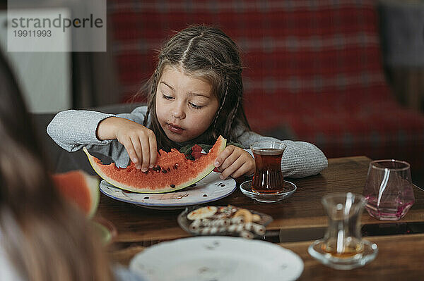 Mädchen isst ein Stück Wassermelone am Tisch