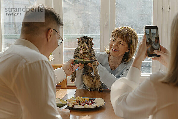 Mann füttert Katze  Frau fotografiert zu Hause per Smartphone