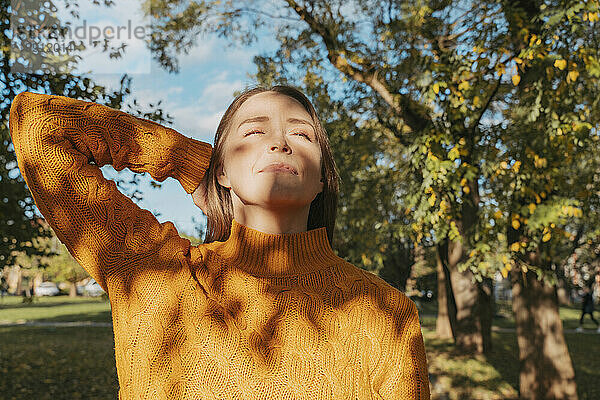 Frau mit geschlossenen Augen genießt das Sonnenlicht im Herbstpark