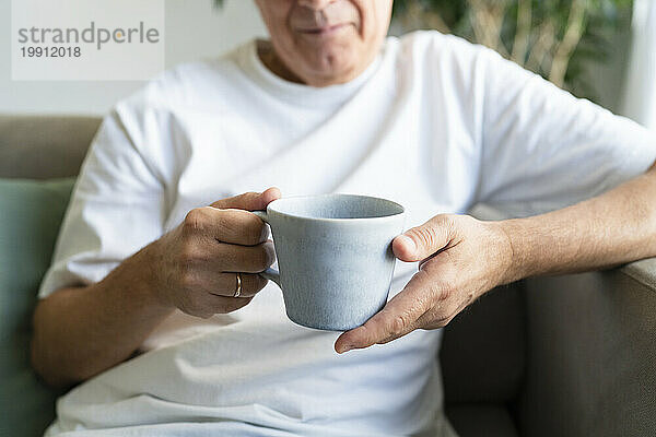 Älterer Mann hält Kaffeetasse im heimischen Wohnzimmer
