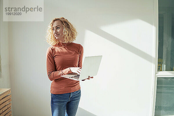 Lächelnde Geschäftsfrau steht mit Laptop im Büro