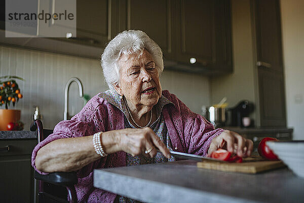 Ältere Frau schneidet Tomaten am Tisch in der Küche