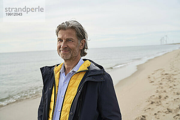 Lächelnder älterer Mann steht am Strand unter freiem Himmel