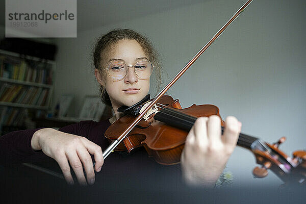 Mädchen trägt eine Brille und spielt zu Hause Geige