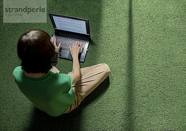 Freiberufler sitzt auf Teppich und benutzt Laptop zu Hause