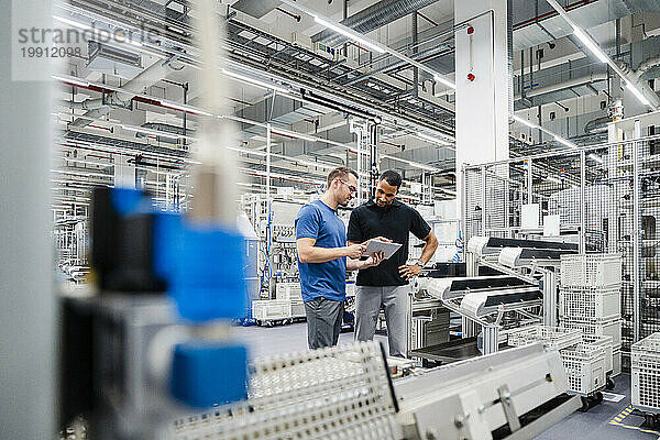 Zwei Kollegen teilen sich in einer Fabrik ein digitales Tablet