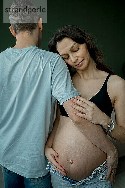 Man and pregnant woman embracing against green background
