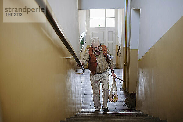 Älterer Mann rückt mit einer Tüte Obst auf der Treppe nach oben