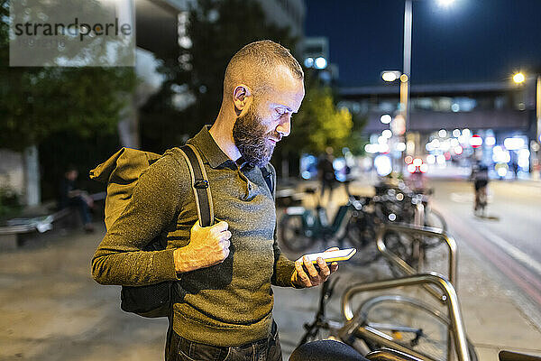 Mann benutzt nachts Smartphone in der Nähe eines Fahrradständers in der Stadt