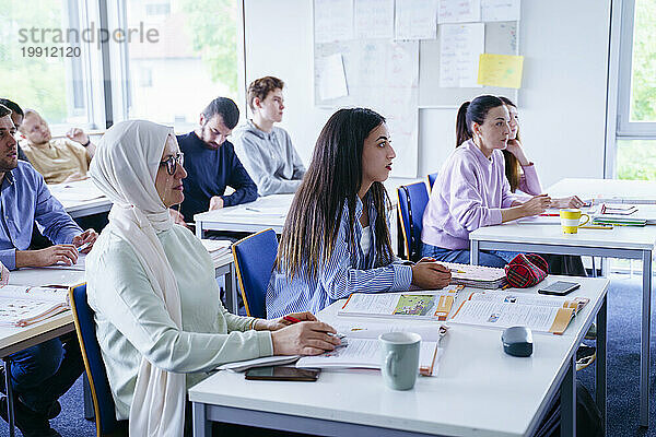 Multiethnische Freunde sitzen an Schreibtischen und besuchen Vorlesungen im Klassenzimmer