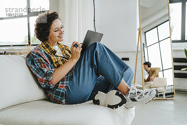 Smiling graphic designer working on tablet PC sitting on sofa at office