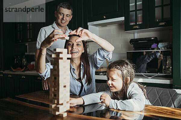 Glückliche Familie  die auf dem Tisch in der Küche ein Blockentfernungsspiel spielt