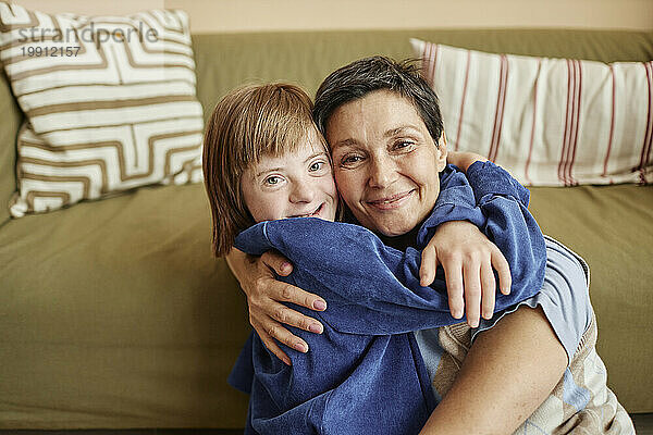 Glückliche Frau und Mädchen mit Down-Syndrom umarmen sich im Wohnzimmer
