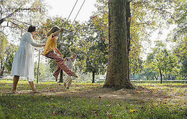 Mädchen schwingt mit Mutter und Bruder  die im Park stehen