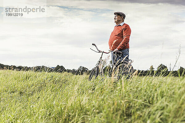 Älterer Mann steht am Fahrrad und blickt auf die Aussicht im Feld