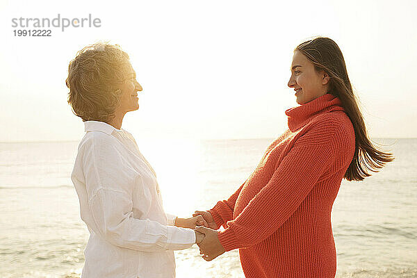 Lächelnde Mutter hält Händchen und steht mit ihrer Tochter am Strand