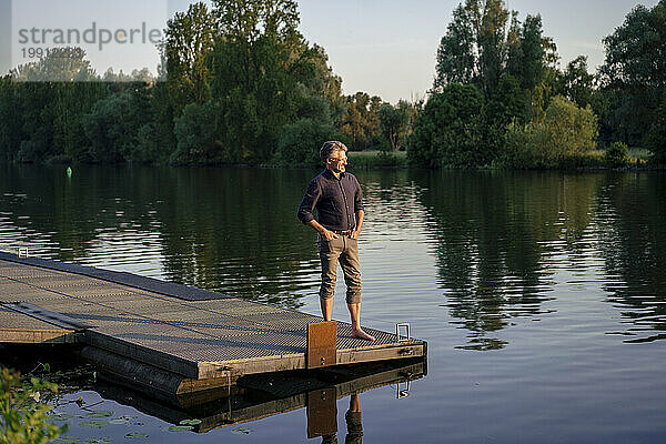 Lächelnder Mann steht auf einem Steg in der Nähe des Sees