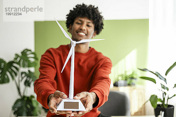 Junger Freiberufler hält Windturbinenmodell im Heimbüro