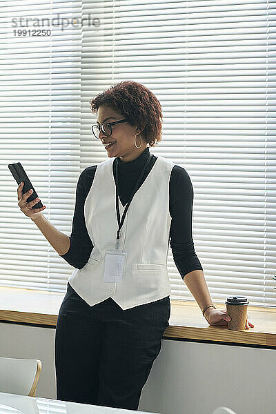 Glückliche junge Geschäftsfrau nutzt Smartphone im Büro