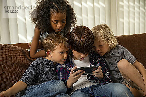 Junge spielt ein Spiel auf dem Smartphone mit Freunden  die auf der Couch sitzen
