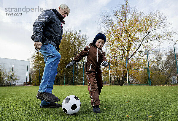 Älterer Mann und Enkel spielen mit Ball auf dem Fußballplatz