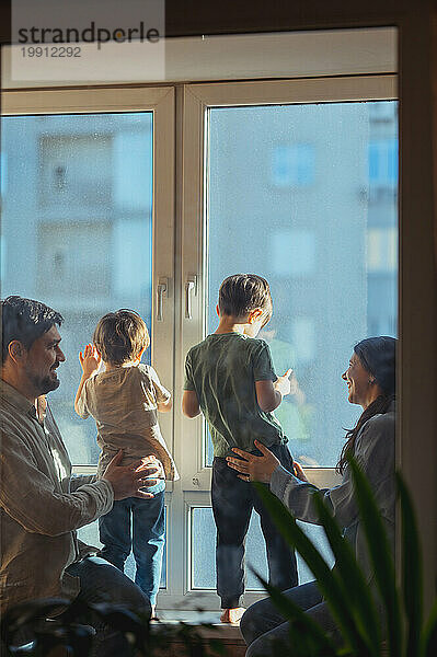 Eltern halten ihre Kinder fest und schauen zu Hause durch das Fenster nach draußen