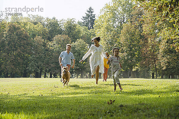 Glückliche Familie läuft mit Hund auf Gras im Park